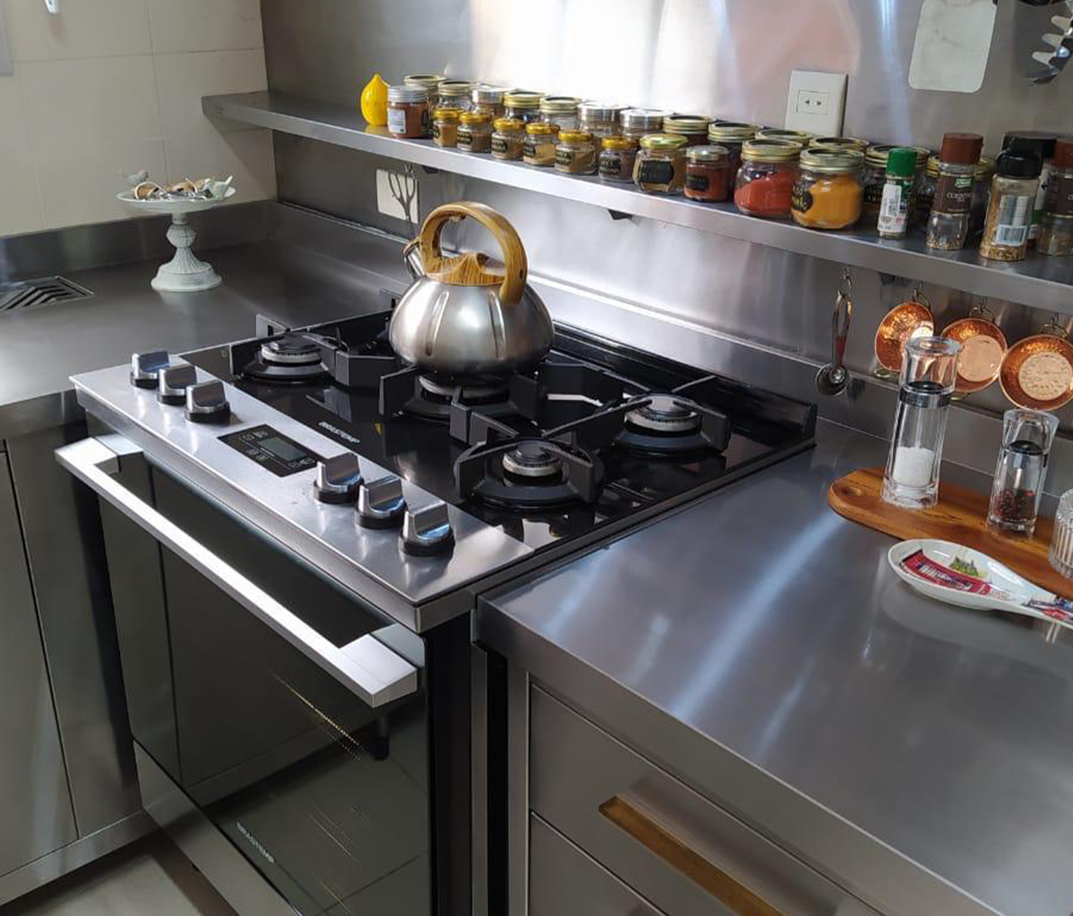 Cozinha residencial com bancada e prateleiras em aço inox, início da marca Santa Ângela.