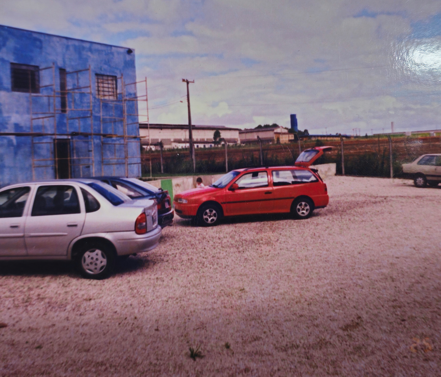 Pátio da fábrica com prédio azul e equipe em expansão, fase de crescimento.